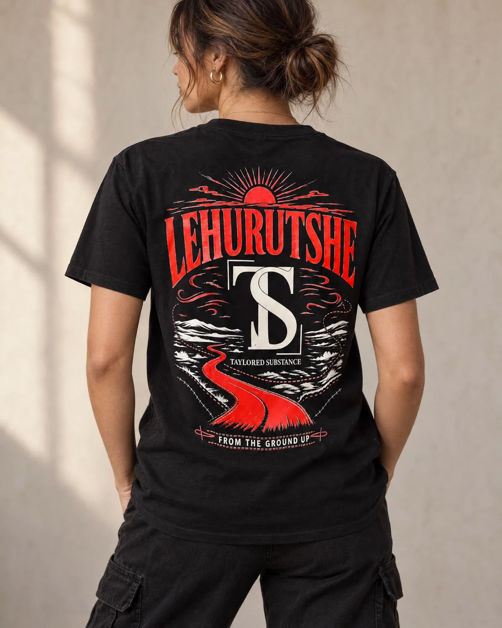 Back view of a model wearing the black tee with a red-and-white Taylored Substance landscape graphic.