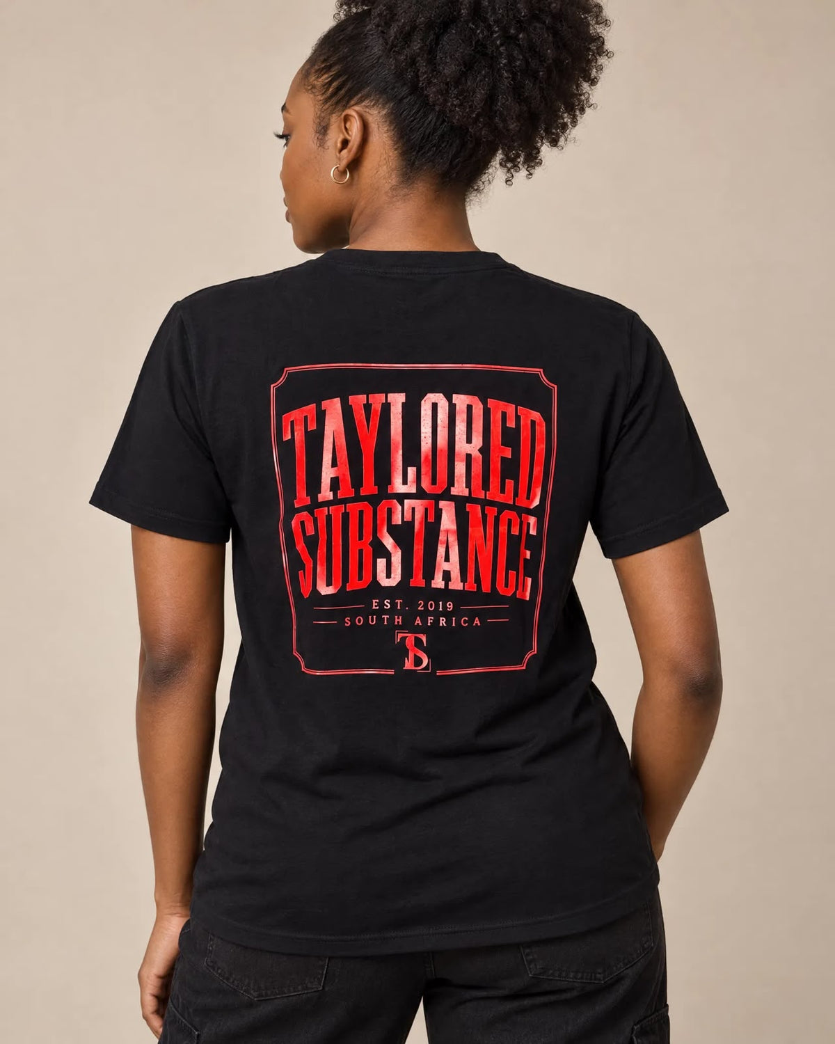 Back view of a model wearing the black T-shirt with the red Taylored Substance graphic.