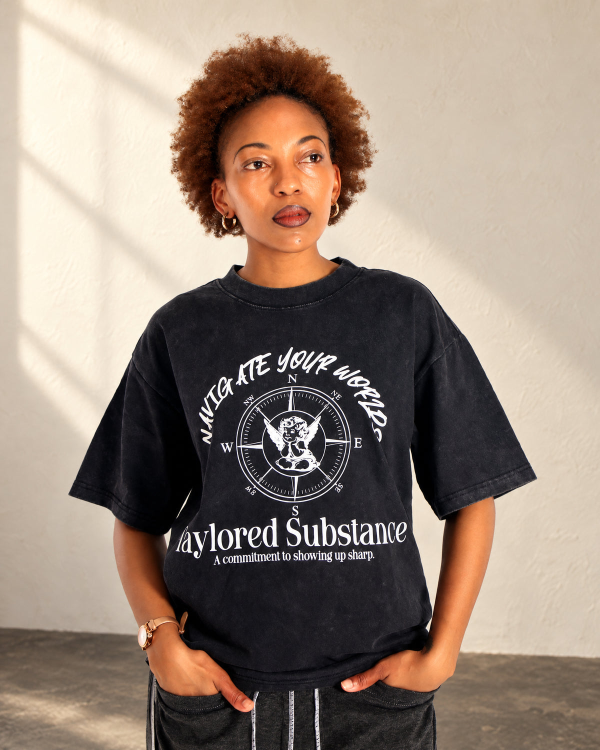 Model wearing the dark stone-washed T-shirt with white Navigate Your Worlds lettering and compass artwork on the front.